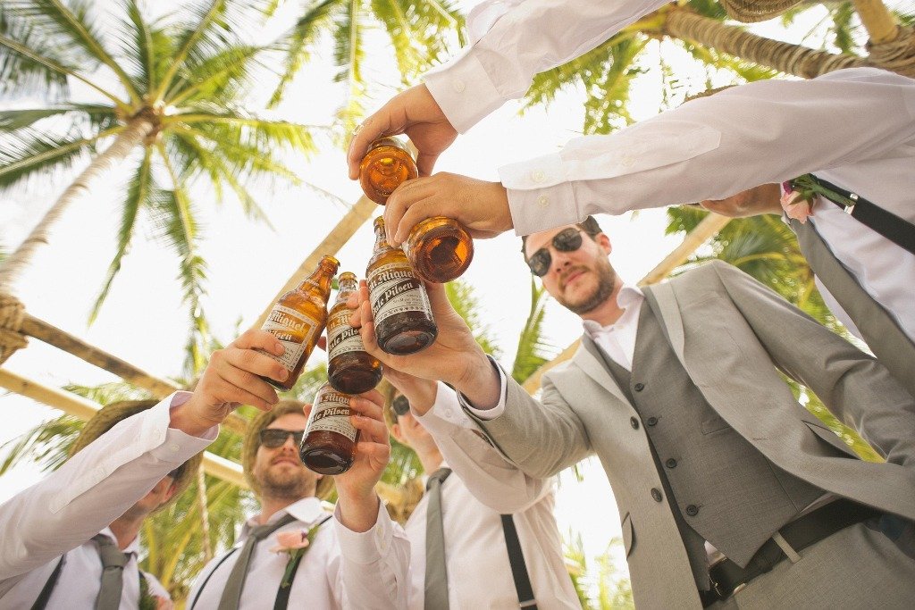 Friends raising beer bottles in celebration toast under palms